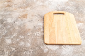 Empty rectangular wooden cutting board on brown concrete background. Side view, copy space