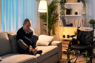 Disabled man sitting on sofa with sad expression in a dark living room