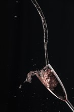 Pink champagne is dynamically poured into a glass, black background