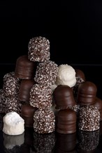 A stack of different chocolate kisses on a dark background with a reflection