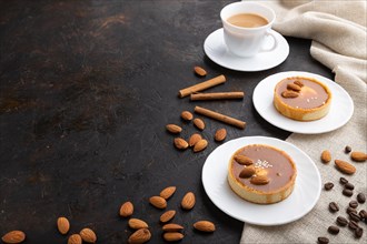 Sweet tartlets with almonds and caramel cream with cup of coffee on a black concrete background and
