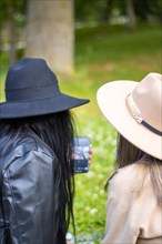 Rear view of two girls looking at the screen of the phone. Back view of two girls in hats looking