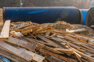 Sections of lumber scattered haphazardly on ground in front of large steel industrial pipes at