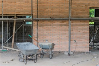 Two gray wheelbarrows in front of red brick wall at construction site