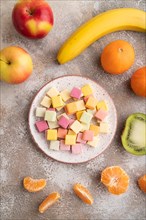 Various fruit jelly chewing candies on plate on brown concrete background. apple, banana,