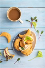 Homemade salted crescent-shaped cheese cookies, cup of coffee on blue wooden background. top view,