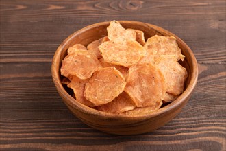 Slices of dehydrated salted meat chips with herbs and spices on brown wooden background. Side view,