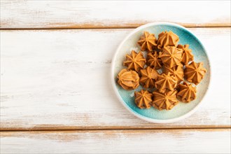 Homemade soft caramel fudge candies on blue plate on white wooden background. top view, flat lay,