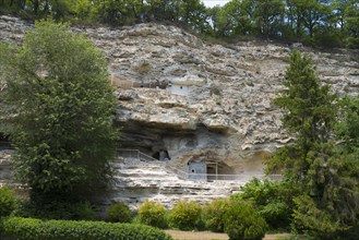 View of cave dwellings in a large rock face surrounded by trees and greenery, Aladja Monastery in 2