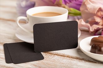 Black business card with cup of cioffee, chocolate candies and iris flowers on white wooden