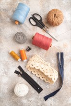 Sewing accessories: scissors, thread, thimbles, braid on brown concrete background. Top view, flat