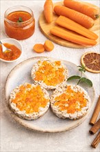 Carrot jam with puffed rice cakes on gray concrete background. Side view, close up