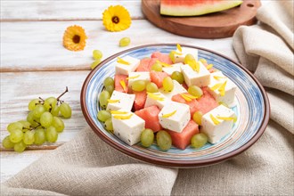 Vegetarian salad with watermelon, feta cheese, and grapes on blue ceramic plate on white wooden