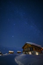 Mountain huts at night under a clear starry sky with illuminated windows in winter, Belalp, Naters,