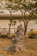 Stone carved statue of Buddhist deity vajraputra in front of white wall in garden in South Korea