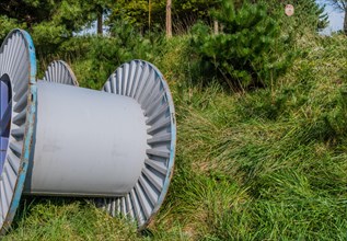 Large metal industrial spools sitting on grassy hillside