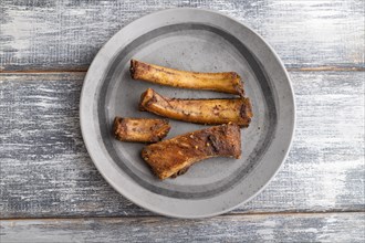 Pork ribs on a wooden plate on a gray wooden background. Top view, flat lay, close up