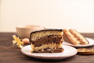 Chocolate biscuit cake with caramel cream, cup of coffee on brown wooden background. side view,