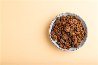 Plate with unrefined brown cane sugar on orange pastel background. top view, flat lay, copy space