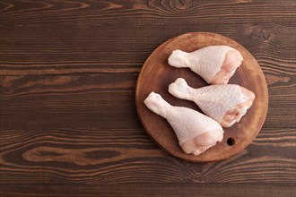 Raw chicken legs on a wooden cutting board on a brown wooden background. Top view, flat lay, copy