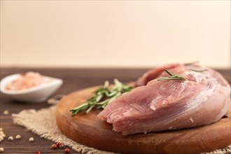 Raw pork with herbs and spices on a wooden cutting board on a brown wooden background. Side view,