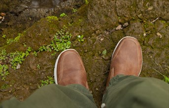 Man feets in hiking leather shoes in outdoors. Top View of shoes on rocky srones near river