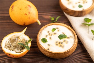 Yoghurt with granadilla and mint in wooden bowl on brown wooden background and linen textile. side