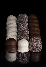 A row of white and dark chocolate kisses on a black background with reflection