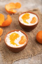 Grained cottage cheese with tangerine jam on brown concrete background and linen textile. side
