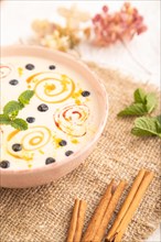 Yoghurt with bilberry and caramel in ceramic bowl on gray concrete background and linen textile.