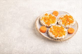Carrot jam with puffed rice cakes on gray concrete background. Side view, copy space