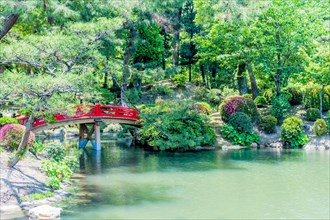 Red wooden footbridge over man made pond in Japanese garden in Hiroshima, Japan, Asia