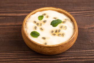 Yoghurt with granadilla and mint in wooden bowl on brown wooden background. side view, close up