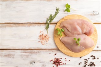 Raw chicken breast with herbs and spices on a wooden cutting board on a white wooden background.