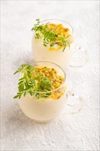 Yogurt with passionfruit and marigold microgreen in glass on gray concrete background. Side view,