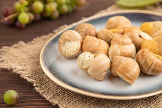 Grape (Burgundy) snails with butter and cheese on brown wooden background and linen textile. Side