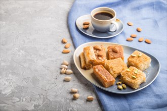 Traditional arabic sweets (basbus, kunafa, baklava) and a cup of coffee on a gray concrete