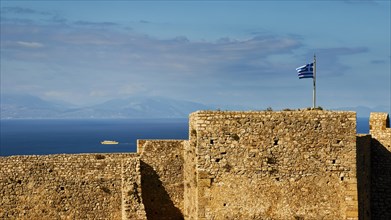 Historic fortress walls under a partly cloudy sky with Greek flag and sea view, Chlemoutsi, High