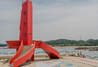 Red lighthouse with curved staircase on concrete dock of seaport in South Korea