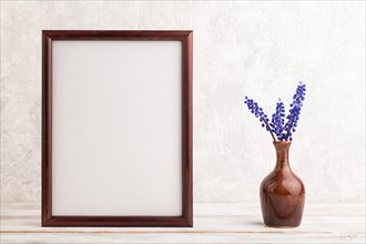 Wooden frame with blue muscari hyacinth flowers in ceramic vase on gray concrete background. side