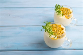 Mango yogurt with passionfruit and cilantro microgreen in glass on blue wooden background. Side