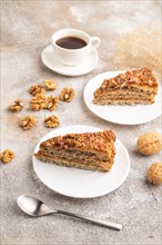 Walnut and hazelnut cake with caramel cream, cup of coffee on brown concrete background. side view
