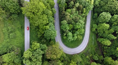Red car driving on serpentine road through green landscape, drone shot, Upper Bavaria, Bavaria,