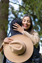 Vertical image of a happy woman hugging her friend with eyes closed in the park while holding her