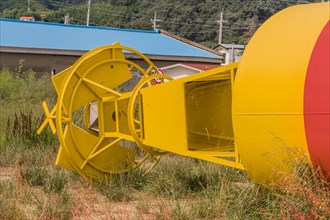 Bottom section of yellow and red ocean buoy laying in grass in fishing village