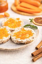 Carrot jam with puffed rice cakes on gray concrete background. Side view, close up, selective focus