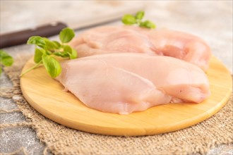 Raw chicken breast with herbs and spices on a wooden cutting board on a brown concrete background.