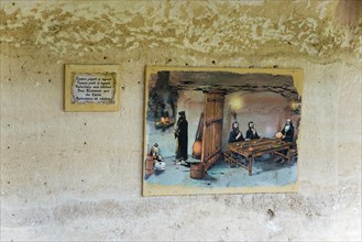 Mural of a historical scene with informative accompanying panel in a cave, dining room and kitchen,