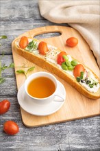 Long white bread sandwich with cream cheese, tomatoes and microgreen on gray wooden background and