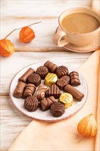 Chocolate candies with cup of coffee and physalis flowers on a white wooden background and orange
